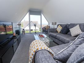 A living room with grey sofas glass coffee table and large window showing house outside at 67 Pendre Avenue in Prestatyn
