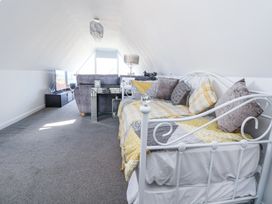 An attic room with a white metal bed, grey sofa, glass side table, television on a black stand and a window at 67 Pendre Avenue Prestatyn