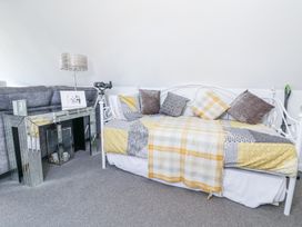 A room with a white daybed with cushions and a yellow patterned blanket next to a mirrored console table with a lamp and telescope at 67 Pendre Avenue in Prestatyn