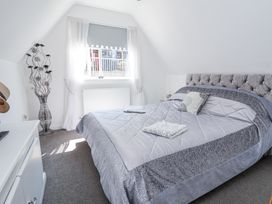 A bedroom with a large bed with folded towels on it a window with curtains a decorative vase and a small cabinet at 67 Pendre Avenue in Prestatyn