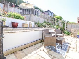 A patio area with wicker furniture and a small table on a rug surrounded by plants and a wooden fence at 67 Pendre Avenue in Prestatyn