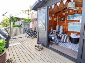 An outdoor wooden deck with a dining table and chairs a large umbrella and a wooden shed with striped lounge chairs and decorations at 67 Pendre Avenue in Prestatyn