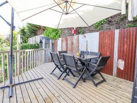 An outdoor wooden deck with a black dining table and six chairs under a large white umbrella at 67 Pendre Avenue in Prestatyn