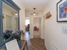 A hallway with a large mirror and flowers on a console table a light fixture on the ceiling and two chairs visible in rooms beyond at Hillside in Bishops Cleeve
