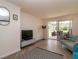 A living room with a TV on a stand a patterned rug a sofa with cushions sliding doors to a conservatory at Hillside in Bishops Cleeve