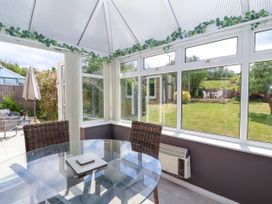 A conservatory with a glass dining table wicker chairs and a view of a garden at Hillside in Bishops Cleeve