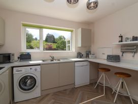 A kitchen with a washing machine, dishwasher, sink, microwave, toaster, kettle, counter stools, and a window with a view of trees and grass at Hillside in Bishops Cleeve
