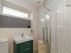 A bathroom with a green vanity and sink a toilet a laundry basket a glass shower enclosure and a frosted window at Hillside in Bishops Cleeve