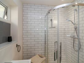 A bathroom with a glass shower enclosure white brick wall tiles a window and a laundry basket at Hillside in Bishops Cleeve