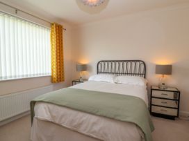 A bedroom with a double bed with green throw and white bedding two bedside tables with lamps and a window with yellow curtains at Hillside in Bishops Cleeve