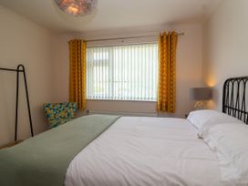 A bedroom with a bed against the wall a window with yellow curtains a chair with a geometric pattern and a lamp at Hillside in Bishops Cleeve