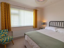 A bedroom with a double bed, a bedside table with a lamp, a patterned chair, and a window with vertical blinds and yellow curtains at Hillside in Bishops Cleeve