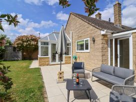 A patio with outdoor furniture and an umbrella next to a stone house with a conservatory and garden at Hillside in Bishops Cleeve