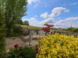 A garden patio area with white plastic chairs and table a stone statue and yellow and red plants at Hillside in Bishops Cleeve