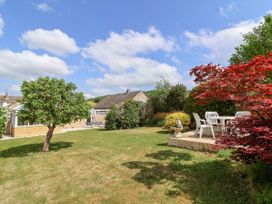A garden with a tree a patio with white chairs and table a house in the background at Hillside in Bishops Cleeve
