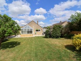 A backyard with a lawn, trees, bushes, and a house with a conservatory at Hillside in Bishops Cleeve