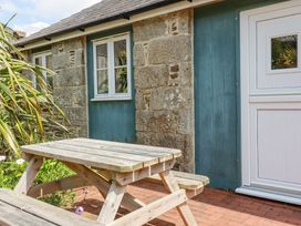 A wooden picnic table outside a stone and blue painted building with a white door at Rose's Stable in Bodrean near Truro