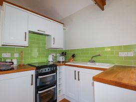 A kitchen with white cabinets green tiled backsplash a black stove a white sink and wooden countertops at Roses Stable Bodrean near Truro