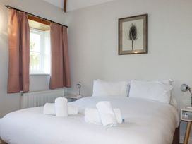 A bedroom with a double bed with white linens and towels a window with pink curtains and framed artwork on the wall at Rose's Stable in Bodrean near Truro
