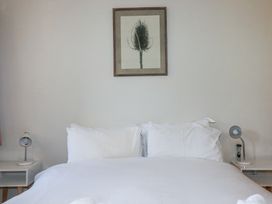 A bedroom with a white bed between two nightstands with lamps and a framed botanical print above the bed at Roses Stable in Bodrean near Truro
