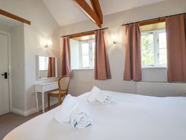 A bedroom with two windows with curtains a white dressing table with a chair and rolled towels on a bed at Rose's Stable in Bodrean near Truro