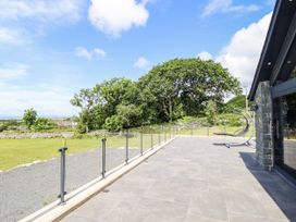 An outdoor patio with glass railing and grass at Perth Y Deri in Llanddwywe