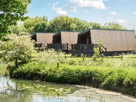 Three wooden cabins with porches near a pond with lilies surrounded by trees and greenery at Billing Aquadrome Holiday Park