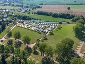An aerial view of a caravan park with multiple caravans on paved plots surrounded by green fields and trees at Nature's Nook Billing Aquadrome in Billing Aquadrome Holiday Park