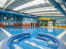 An indoor swimming pool area with a hot tub a yellow water slide and wall murals at Nature's Nook - Billing Aquadrome in Billing Aquadrome Holiday Park