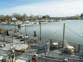 Outdoor dining area with tables and chairs on wooden deck overlooking a marina with boats and houses in the background at Nature's Nook - Billing Aquadrome