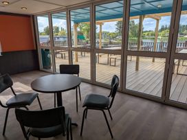 A room with a round table and four chairs near large glass doors opening onto a deck with tables and chairs by the water at Nature's Nook - Billing Aquadrome