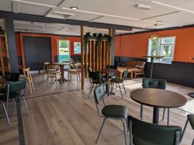 An indoor dining area with multiple round tables and chairs wooden floor and orange and black walls at Natures Nook Billing Aquadrome