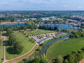 An aerial view of a campsite with rows of caravans near a river and a lake with boats at Meadowview Billing Aquadrome in Billing Aquadrome Holiday Park