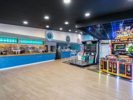 An indoor area with a blue bar counter and arcade machines on a wooden floor at Meadowview - Billing Aquadrome in Billing Aquadrome Holiday Park
