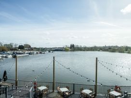 An outdoor seating area with tables and chairs overlooking a body of water with boats docked and string lights hanging at Meadowview - Billing Aquadrome in Billing Aquadrome Holiday Park