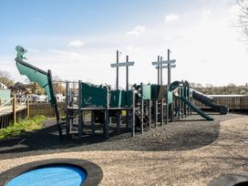 An outdoor playground with a ship-themed climbing structure slides and a small trampoline at Meadowview - Billing Aquadrome in Billing Aquadrome Holiday Park
