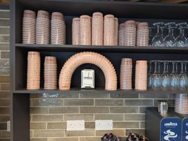 Shelves with stacks of pink paper cups and wine glasses above a tiled kitchen wall