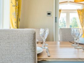 A dining table with wine glasses and cutlery with upholstered chairs and yellow floral curtains at Serenity Shores -  Billing Aquadrome in Billing Aquadrome Holiday Park