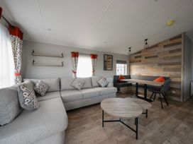 A living room with a grey sectional sofa and patterned cushions a wooden coffee table a dining table with bench seating and a wood panel wall at Billing Bliss - Billing Aquadrome in Billing Aquadrome Holiday Park