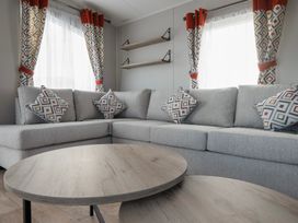 A living room with a grey sectional sofa with patterned cushions and matching curtains with two wooden round coffee tables at Billing Bliss - Billing Aquadrome in Billing Aquadrome Holiday Park