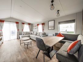 A living room with a grey sectional sofa a wooden dining table with chairs and patterned curtains at Billing Bliss - Billing Aquadrome in Billing Aquadrome Holiday Park