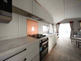 A kitchen with countertop gas stove oven and sink next to a living area with curtains and coffee tables at Billing Bliss Billing Aquadrome Holiday Park