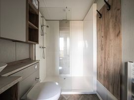 A bathroom with a shower area a toilet a wooden cabinet and a wall with hooks at Billing Bliss - Billing Aquadrome in Billing Aquadrome Holiday Park