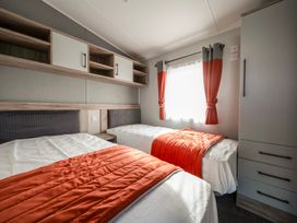 A bedroom with two single beds orange blankets gray and orange curtains and built in cabinets at Billing Bliss - Billing Aquadrome in Billing Aquadrome Holiday Park