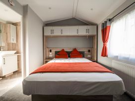 A bedroom with a double bed with orange cushions and bed runner and overhead cabinets at Billing Bliss Billing Aquadrome Holiday Park