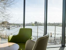 A seating area with a green chair and a beige chair by a window overlooking a lake with boats and string lights at Tranquil Waters - Billing Aquadrome