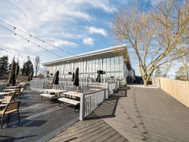 An outdoor seating area with wooden tables and benches under string lights next to a glass building with trees around at Tranquil Waters - Billing Aquadrome