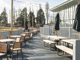 An outdoor patio area with wooden tables and chairs next to a modern building with glass walls at Tranquil Waters - Billing Aquadrome in Billing Aquadrome Holiday Park