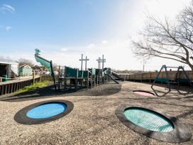 An outdoor playground with a ship-themed climbing structure slides swings and three circular trampolines at Tranquil Waters - Billing Aquadrome in Billing Aquadrome Holiday Park