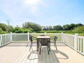 An outdoor deck with a table and four chairs overlooking green trees at Tranquil Waters - Billing Aquadrome in Billing Aquadrome Holiday Park
